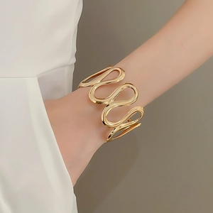 Close-up of golden wavy cuff bracelet with mirror-polished finish on female model