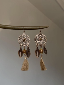 Détail de boucles d'oreilles bohèmes avec feuilles de bronze et longs pompons beiges