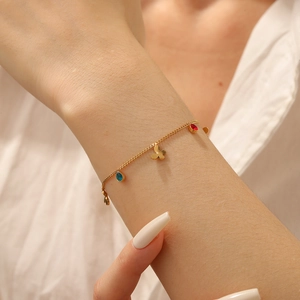 Close-up of gold-plated bracelet with butterfly charm and colorful zircon stones on wrist