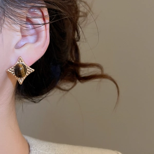 Close-up of vintage gold starburst stud earring with oval tiger eye stone on ear