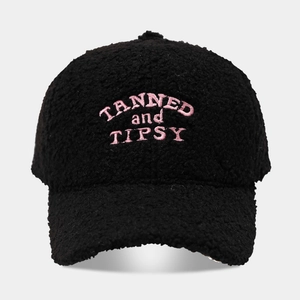 Close-up of pink TANNED and TIPSY embroidery on a black sherpa fleece baseball cap