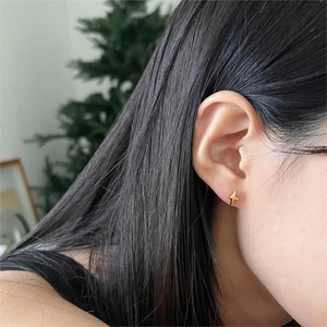 Close-up of a minimalist gold star stud earring worn on ear with cozy blurred background