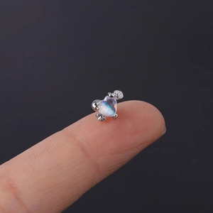 Macro view of tiny heart-shaped blue zircon stud earring placed on a fingertip