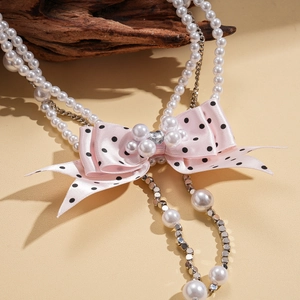 Detail of multi-layer pearl necklace with pink polka dot ribbon bow and heart crystal