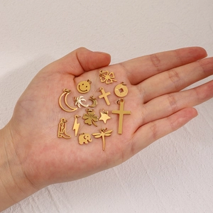Hand holding various gold stainless steel charms including clover, star, and moon shapes