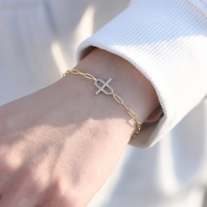 Close-up of gold paperclip chain bracelet with zircon cross charm on woman's wrist