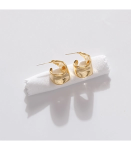 Close-up of gold-plated minimalist C-shaped hoop earrings on white fabric background