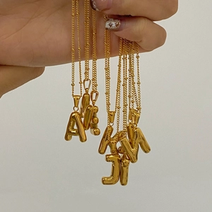 Close-up of chunky gold 3D initial letter pendants on delicate beaded chains