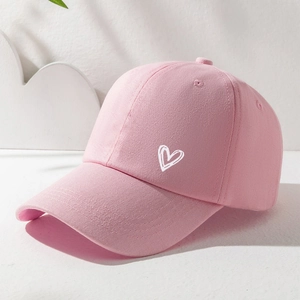 Close-up of a pink cotton baseball cap featuring a white heart embroidery on a soft surface