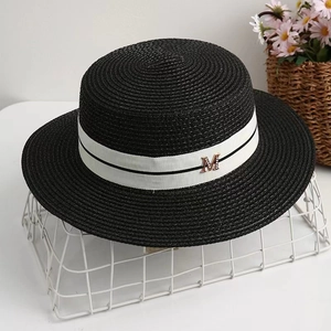 Détail d'un canotier en paille noire avec ruban blanc et logo en métal doré rose lettre M