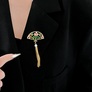 Detailed close-up of fan-shaped enamel brooch with pearl and tassels on a black suit jacket
