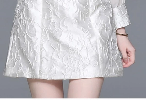 Detailed close-up of white embossed floral jacquard fabric texture on a vintage dress