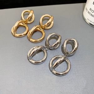 Dettaglio macro di orecchini a cerchio intrecciati in finiture oro e argento lucido