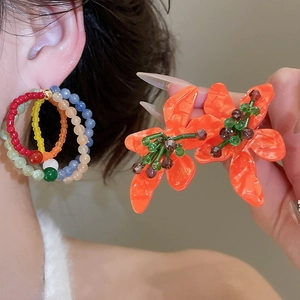 Detail of colorful beaded hoops and orange flower stud earrings with green accents