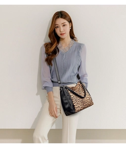 Detail of leopard print panel on black leather handbag worn by model against a white wall