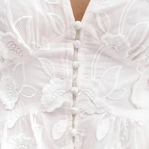 Détail de la broderie florale et des boutons en tissu sur la robe blanche à col en V