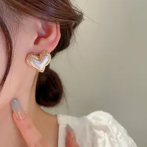 Elegant gold heart earrings with pearl inlay shown from a side-view on a model