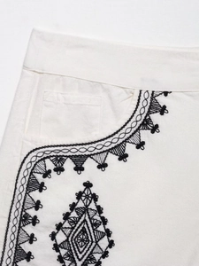 Close-up of geometric black embroidery on white linen shorts with intricate pocket detail