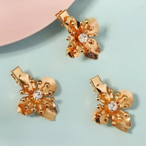 Three gold flower hair clips with sparkling crystal centers on blue and pink background