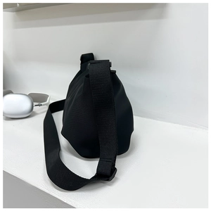Detail view of a minimalist black pleated dumpling crossbody bag on a white surface with headphones