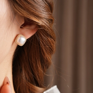 Close-up of elegant gold plated pearl earrings with zircon inlay worn by a model
