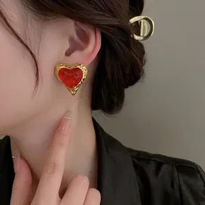 Vintage gold hammer-textured heart earrings with vibrant red enamel on a model