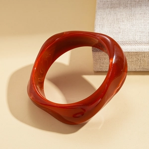 Detailed view of red-brown resin bangle featuring a wavy edge and sand-like texture
