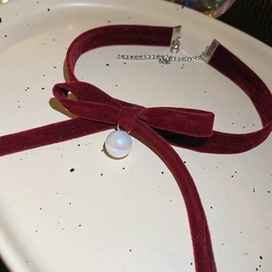 Close-up of a burgundy velvet bow necklace featuring a radiant aurora pearl pendant