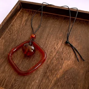 Collier vintage avec pendentif carré en résine ambre sur plateau en bois naturel