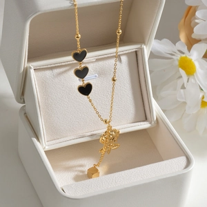 Detail of gold necklace featuring black hearts, rose pendant and square cube on jewelry box