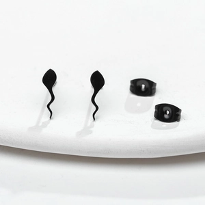 Macro shot of minimalist black tadpole-shaped stud earrings on a white ceramic plate