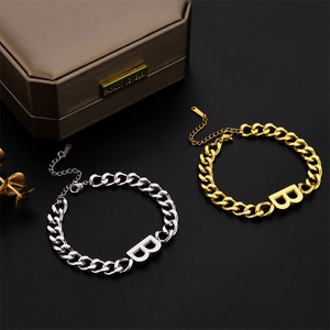 Macro detail of chunky gold and silver chain bracelets featuring a bold letter B charm