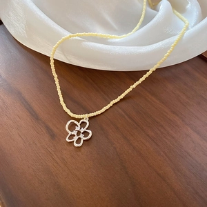 Collana di perle gialle con ciondolo a fiore e zirconi su legno scuro e seta bianca
