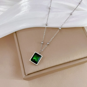 Close-up of minimalist silver titanium necklace featuring a green emerald pendant on box