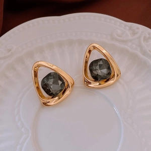 Detail of gold triangle earrings with dark grey crystal on a textured ceramic plate