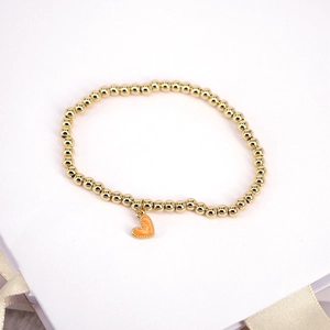 Close-up of golden beaded stretch bracelet featuring a vibrant orange heart pendant