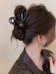Detail of a large amber-textured hair claw and golden twist hoop earring on a model