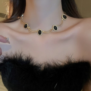 Close-up of a vintage gold necklace featuring five black oval gems on a model