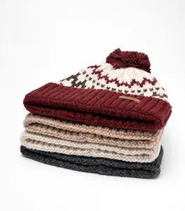 Vertical stack of four thick knitted wool beanies with soft pom-poms in diverse colors