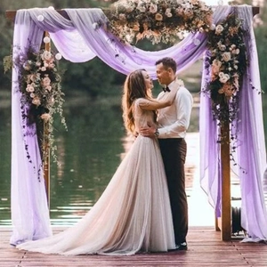 Close-up of purple chiffon fabric draped over wooden wedding arch with floral decor