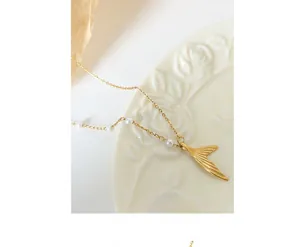 Detail of gold mermaid tail pendant necklace featuring small pearls and brushed metal finish