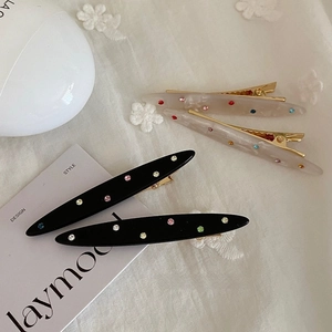 Set of four colorful rhinestone acetate hair clips with gold metal base on white fabric