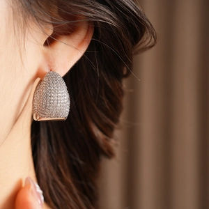 Close-up of C-shaped hoop earrings with pave-set zircon stones on a model ear