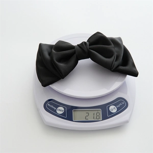 Detail shot showing a black satin layered bow hair clip weighing 21.8g on a digital scale