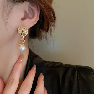 Close-up of vintage gold embossed round earrings with white pearl pendant on model