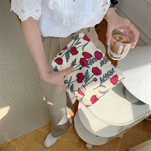 Close-up of floral cotton pouch held by hand featuring red poppy print on beige fabric