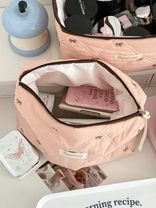 Top view of a pink quilted cosmetic bag featuring brown bow embroidery and a zipper closure