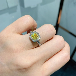 Close-up of a square cut yellow diamond ring with a halo of white zircon on finger