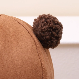 Detail of winter trapper hat with caramel faux suede texture and a plush yarn pom-pom