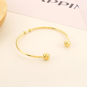 Detail view of a gold-plated C-shaped cuff bracelet with spheres on a minimalist background